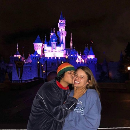 Xolo Maridueña kissing Hannah Kepple on the cheek in front of the Disneyland princess castle.